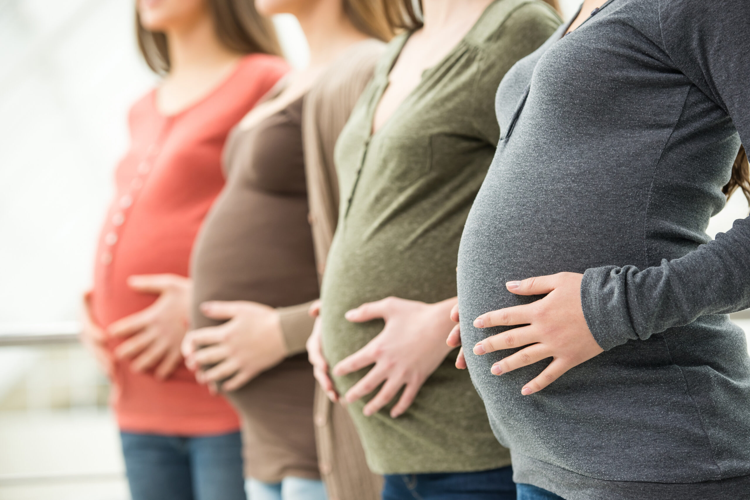Vier schwangere Frauen in einer Reihe mit Händen auf dem Bauch