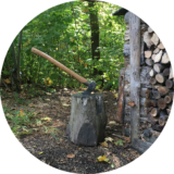 Handwerk und Natur: Hauklotz mit Beil vor einem Holzstapel im Wald