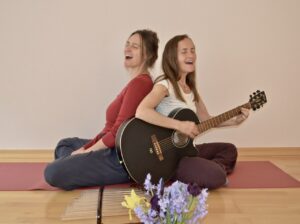 Sonja und Janine singend mit Gitarre auf der Yogamatte