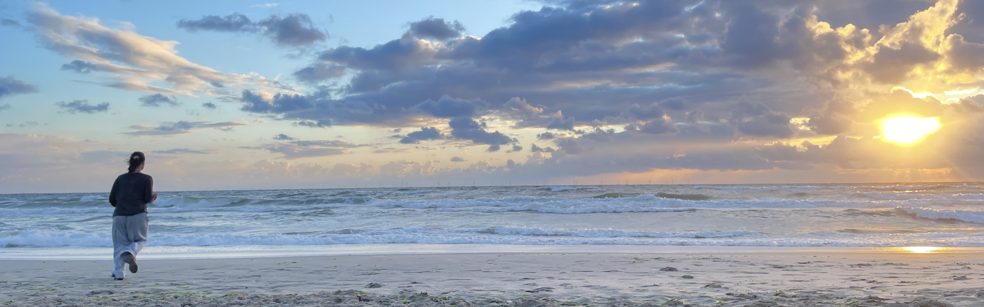 Titelbild: Junge Frau am Strand im Wind in der untergehenden Sonne