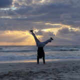 Frau schlägt Rad am Strand im Sonnenuntergang